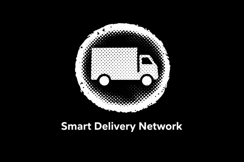 An audience sitting in dark folding chairs, clapping enthusiastically. Several people wearing name tags are visible in the front row, illuminated by stage lighting.